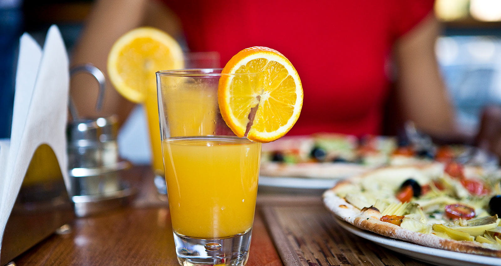 A woman enjoys a glass of orange juice and a breakfast pizza at a café