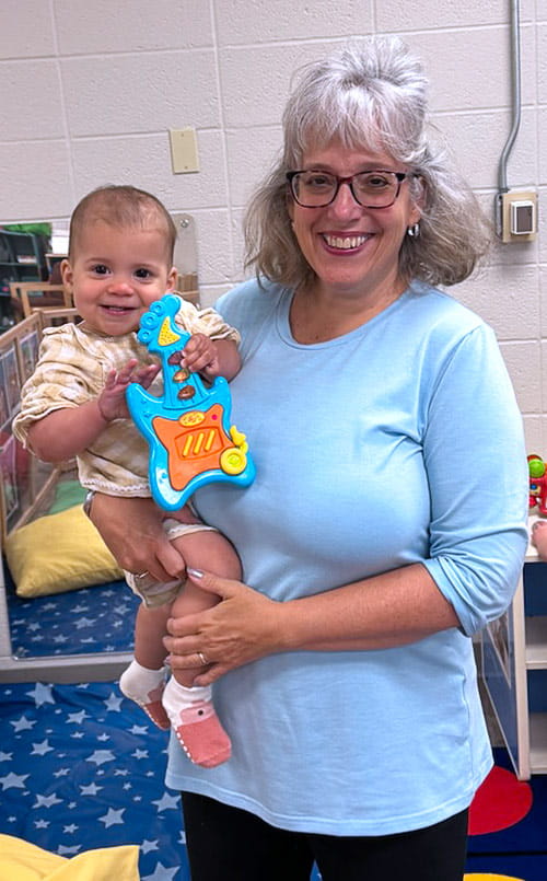 A smiling woman holds an infant at the Child Care Center at UH Parma Medical Center