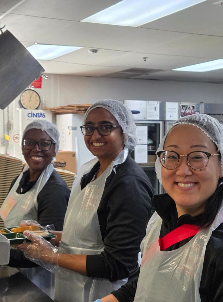 three residents with hair caps on cooking meals