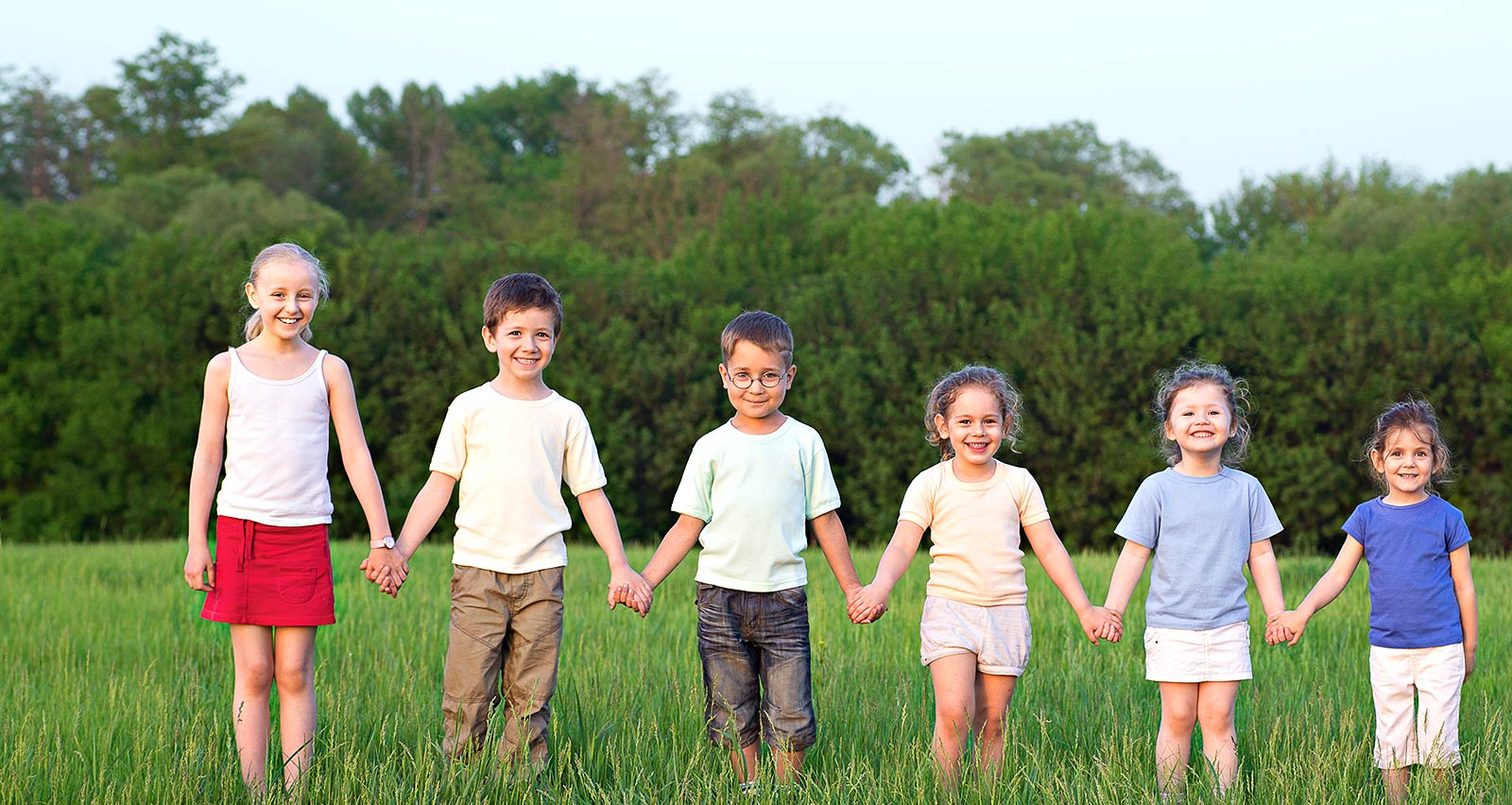 Six children, ranging in ages, holding hands in a field