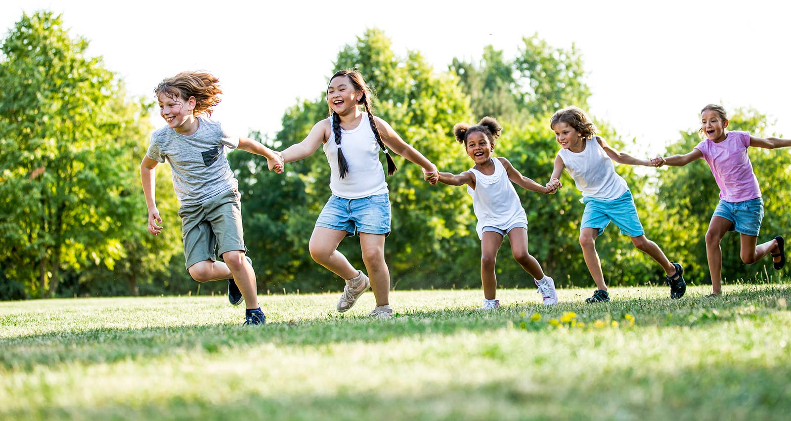 A diverse group of children holding hands and running in a park