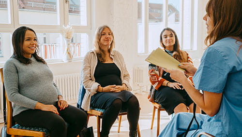 Three pregnant women sitting in chairs listening to a nurse reading from a list before their prenatal tour at University Hospitals.