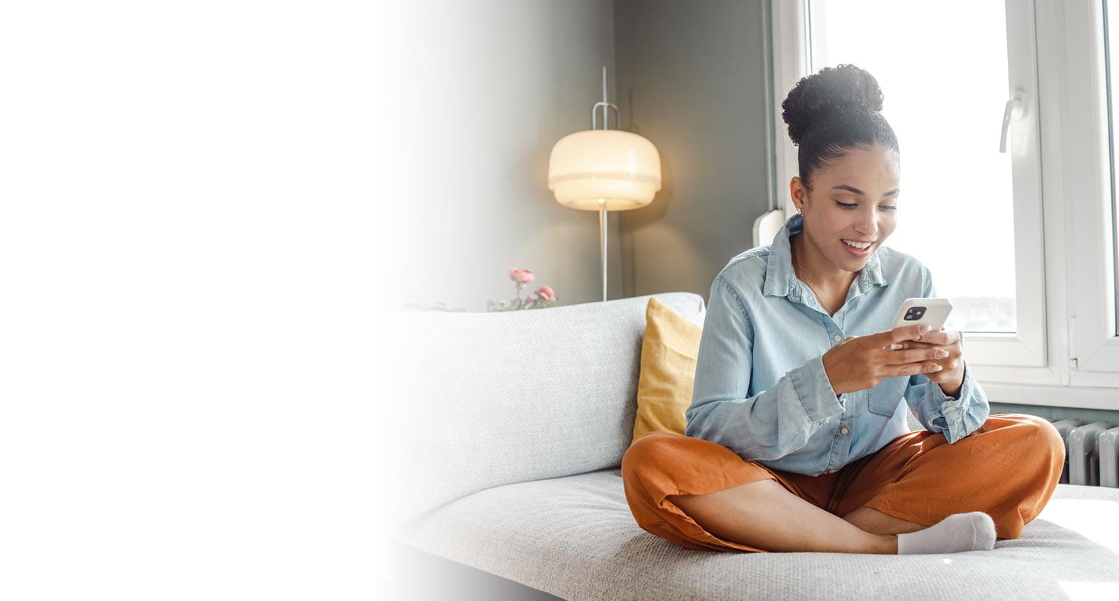 Young woman sitting on a couch shopping on her phone.