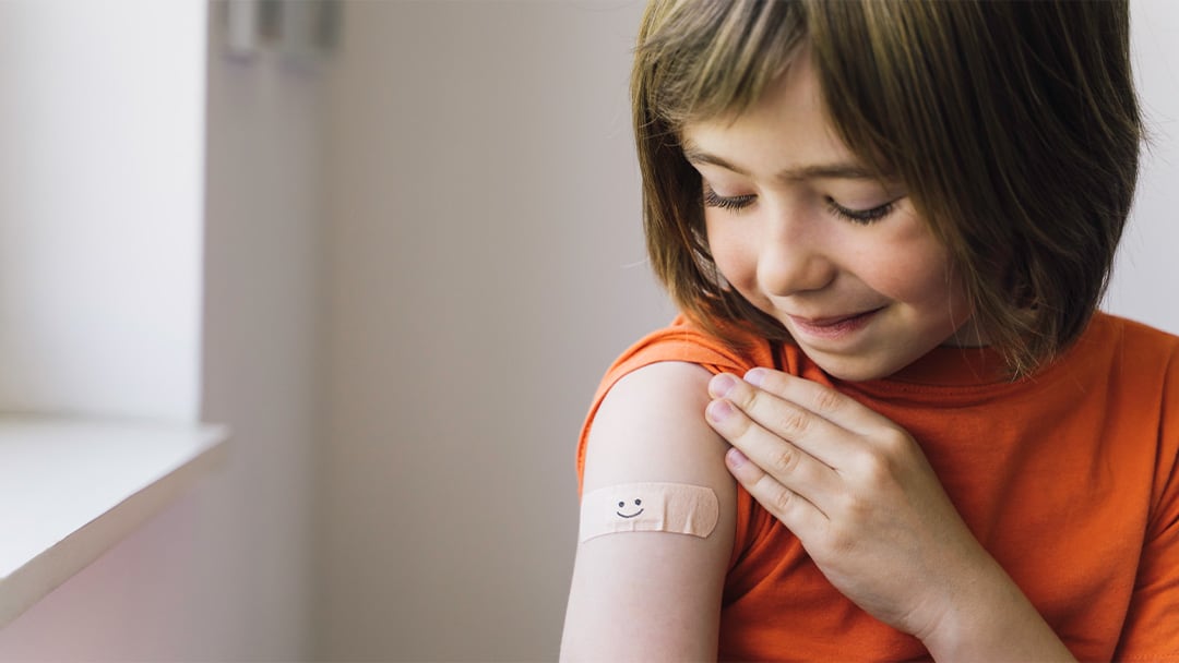 A young girl observes her vaccination band-aid with joy, illustrating a moment of personal triumph and the emotional connections children form with their health journeys