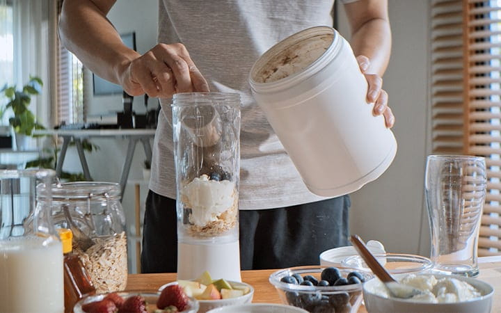 man adding protein powder to a smoothie in a blender