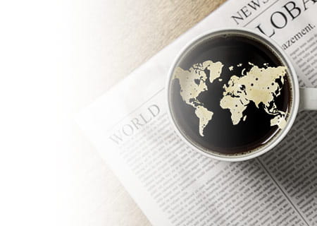 Overhead shot of a cup of coffee with world map in cream on a world newspaper on top of a wood table with a soft shadow