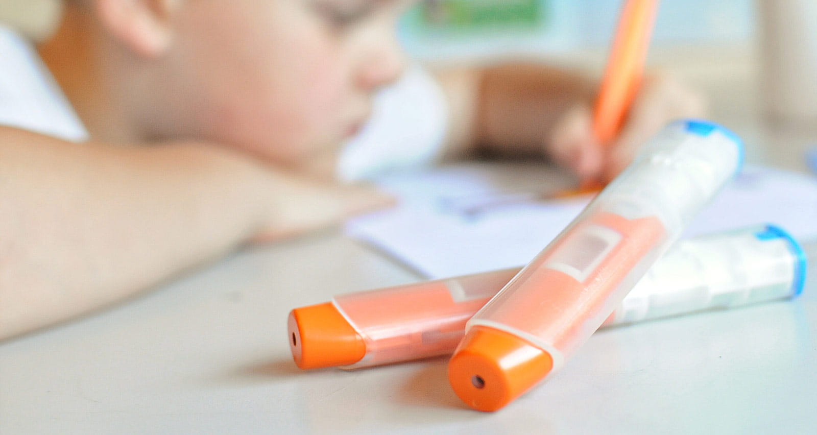 A young boy doing homework with epipens in the foreground
