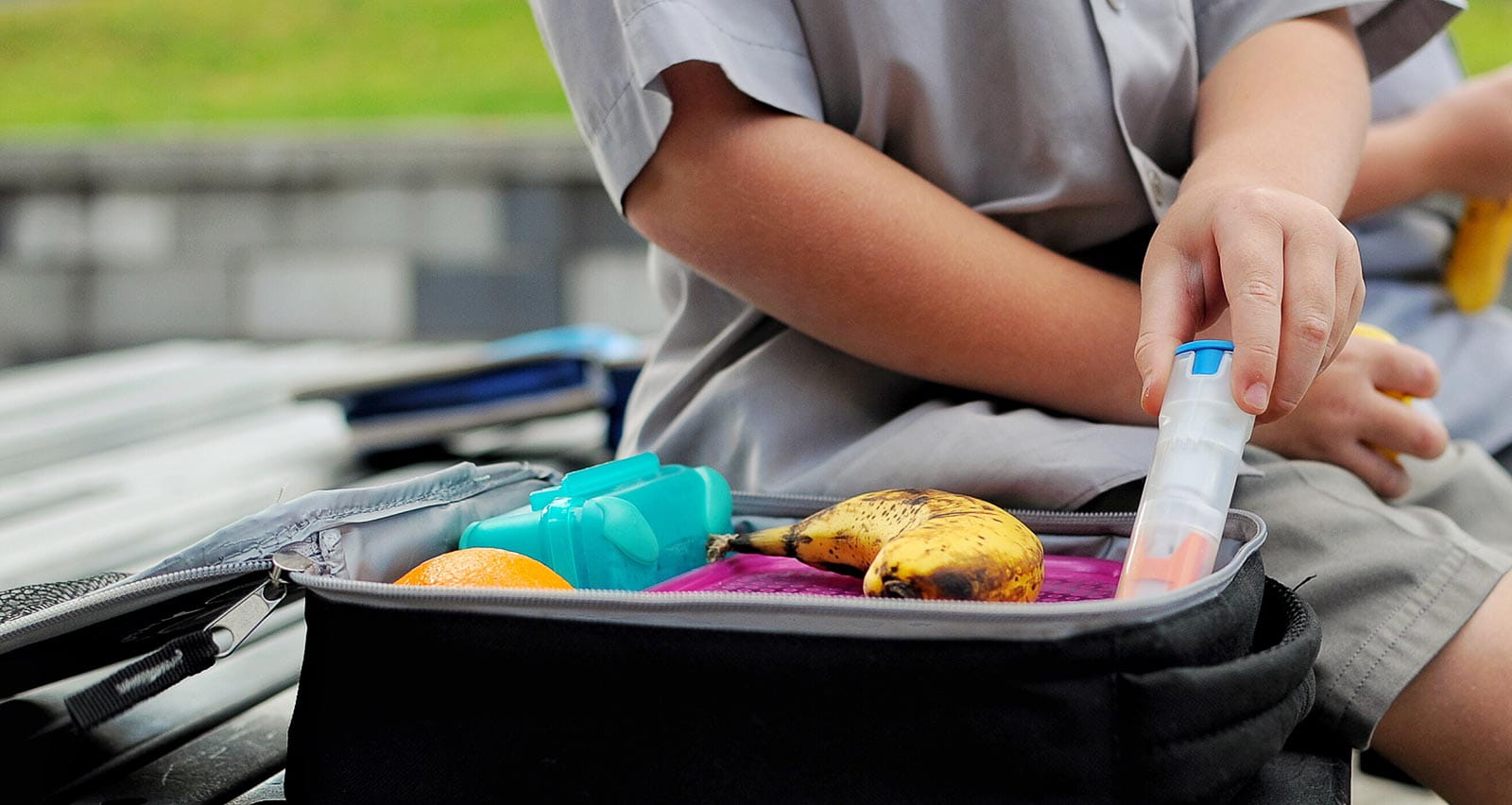 A young boy with a packed lunch takes out his anaphylaxis auto injector