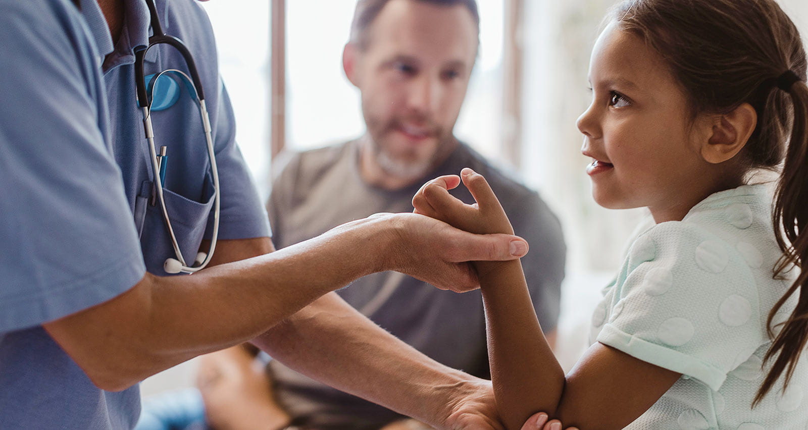 A nurse examining girl sitting with father at clinic