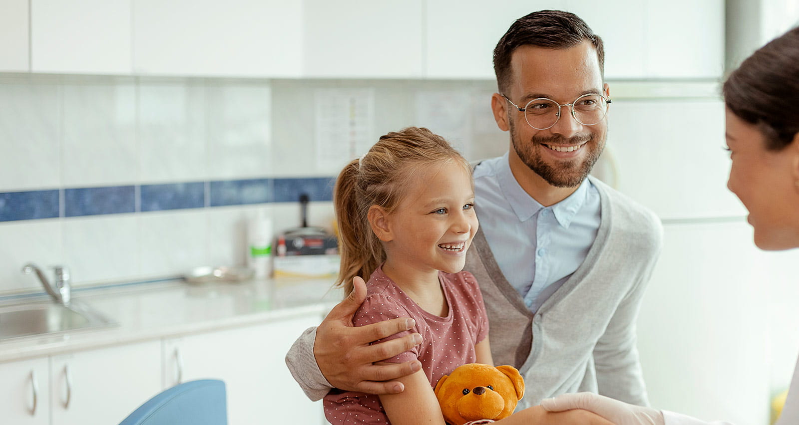 A smiling little girl and her father shaking hands with a friendly female pediatrician at hospital