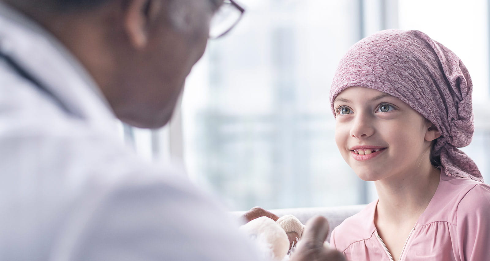 A girl with leukemia sits near a window while meeting with her doctor