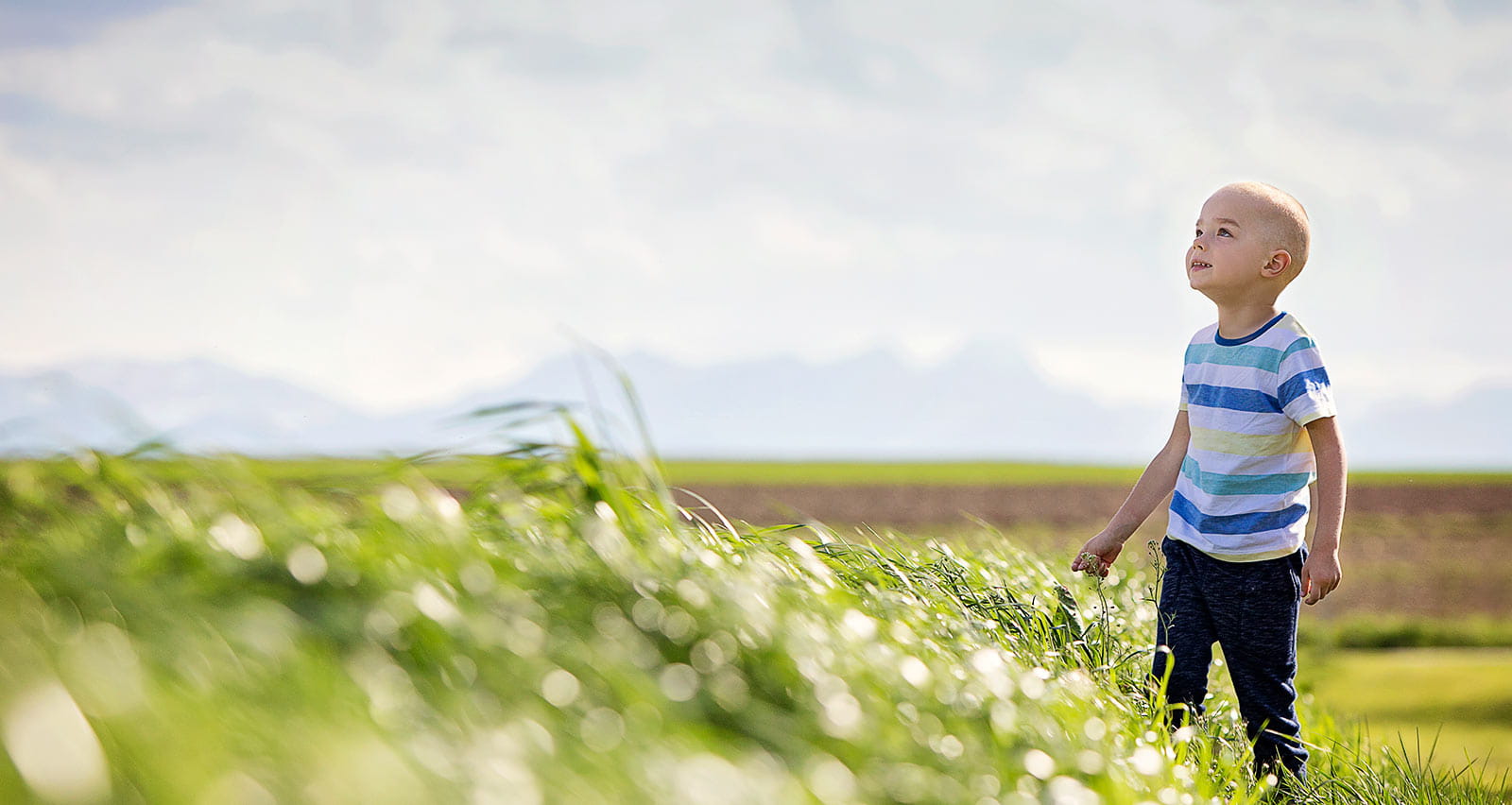 A young cancer patient is in a grassy field on a brilliant sunny day