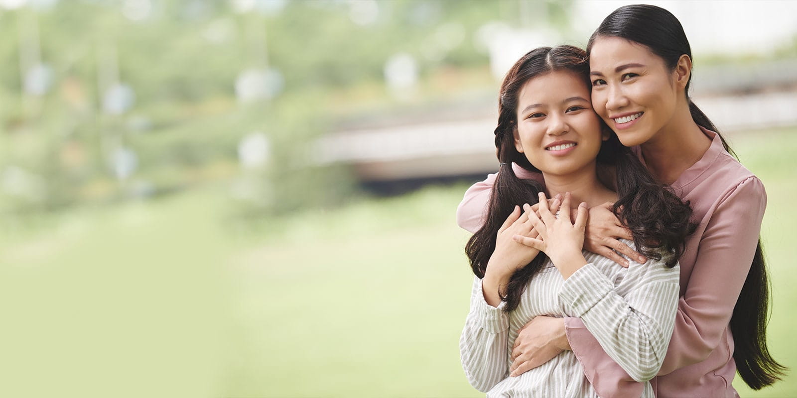 Mother and daughter embracing outside in a park.