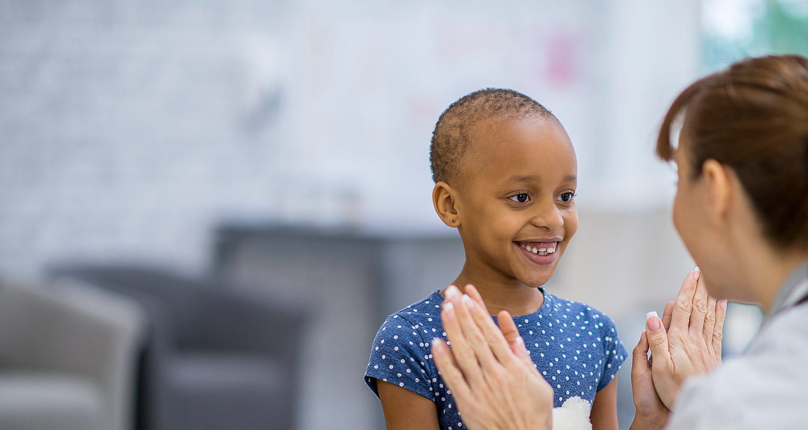 A young cancer patient smiles and gives a high-five to her doctor