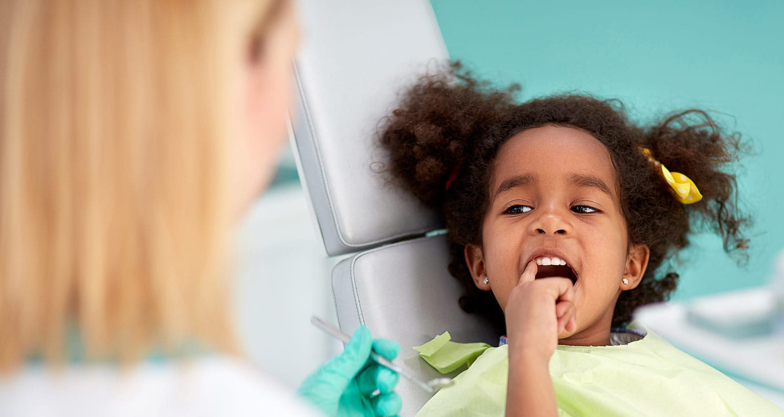 A young girl in a dental chair points to an aching tooth