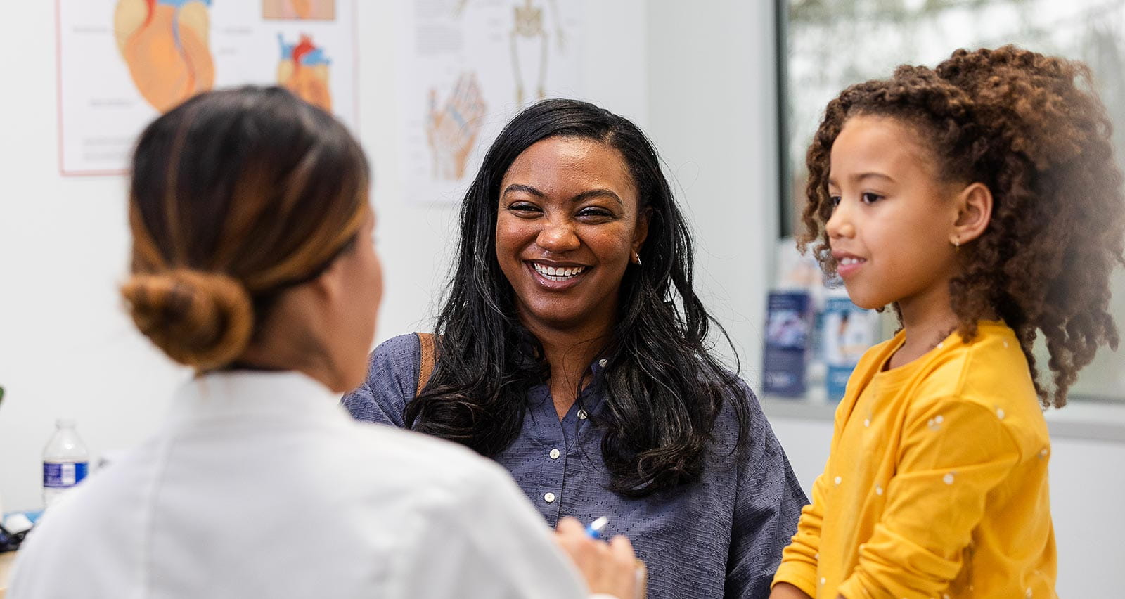A mother and her young daughter smile while listening to the pediatrician