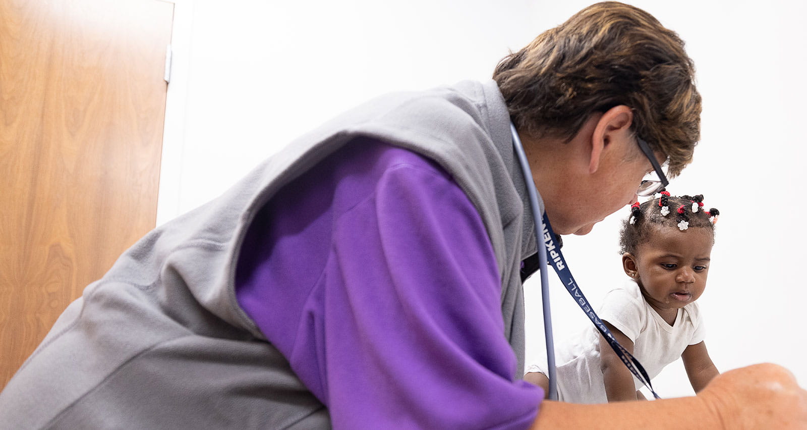 A baby smiles on the exam table while watched over by a UH provider