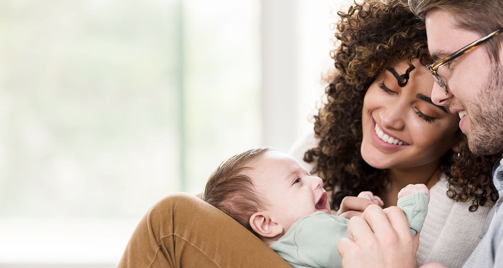 A happy young woman and her husband smile at their laughing newborn baby boy