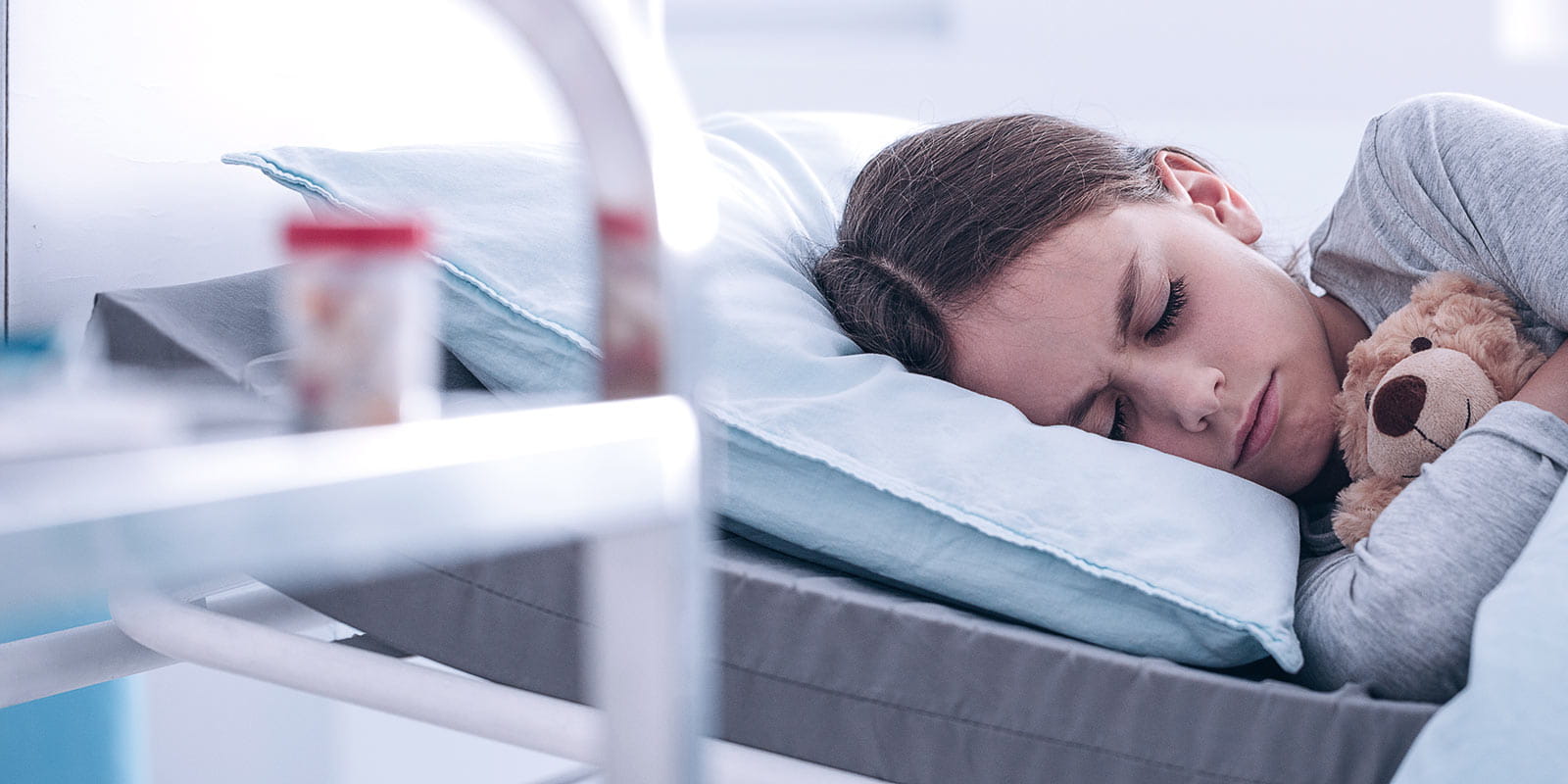 Restless girl hugging teddy bear while lying in hospital bed