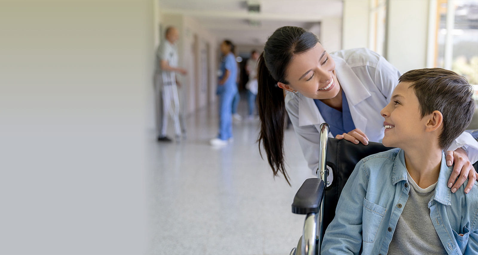 A female doctor greeting a young patient in a wheelchair at the hospital on his way to be discharged