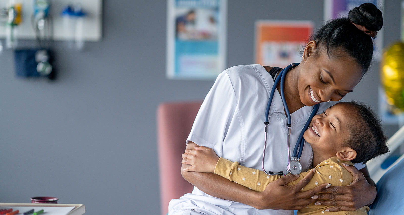 A pediatric patient sits on the edge of his hospital bed as he gives his provider a warm hug