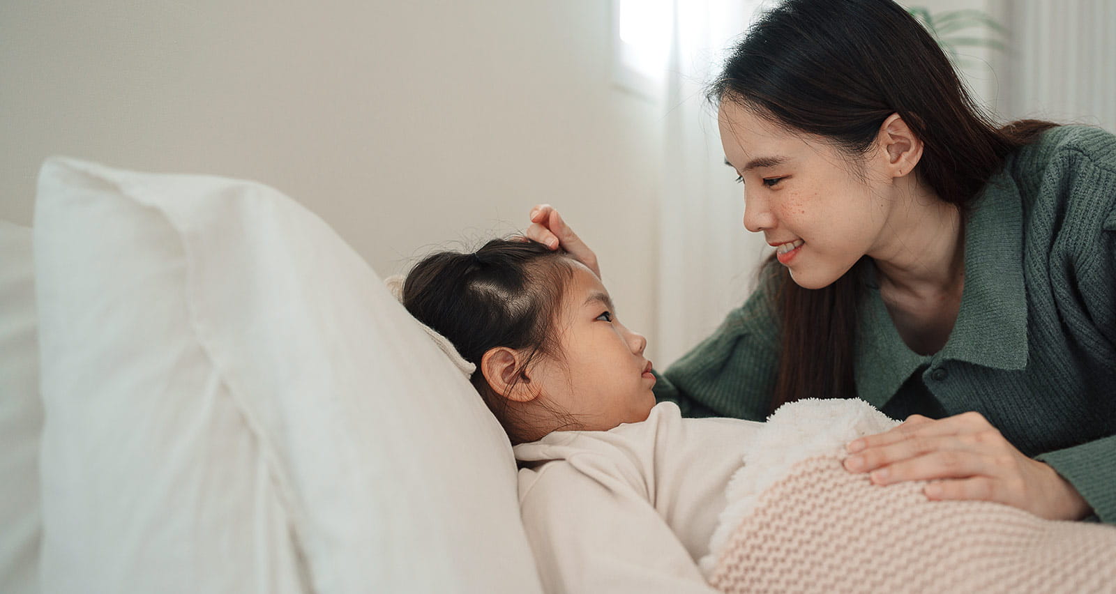 A concerned mom measuring her sick daughter's temperature while she rests in bed