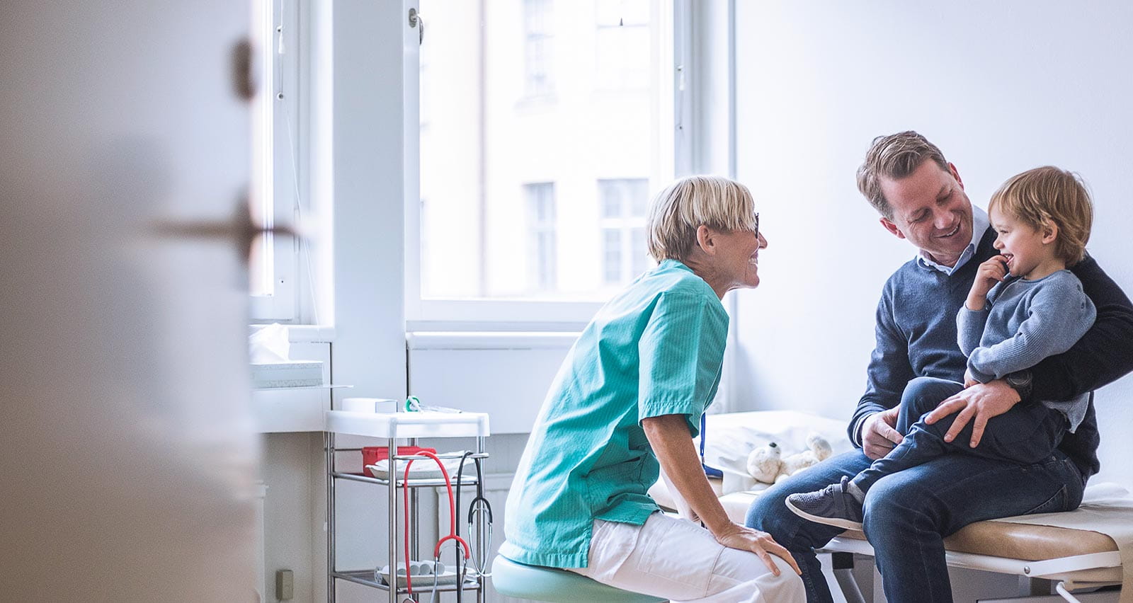 Side view of a smiling female doctor talking to a boy and his father in a clinic