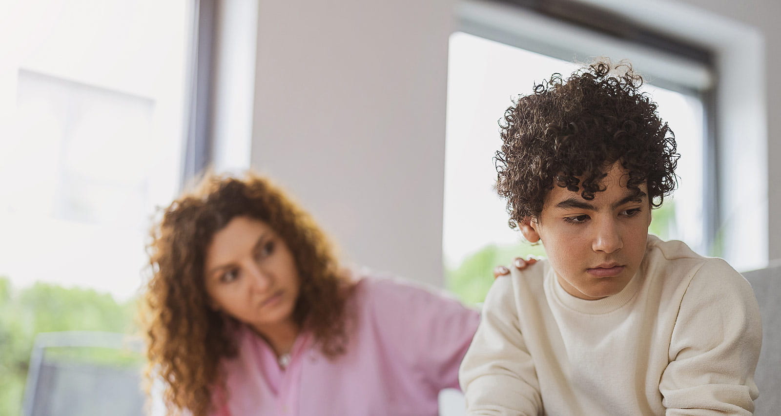 An upset boy sitting on a sofa while his mother looks at him