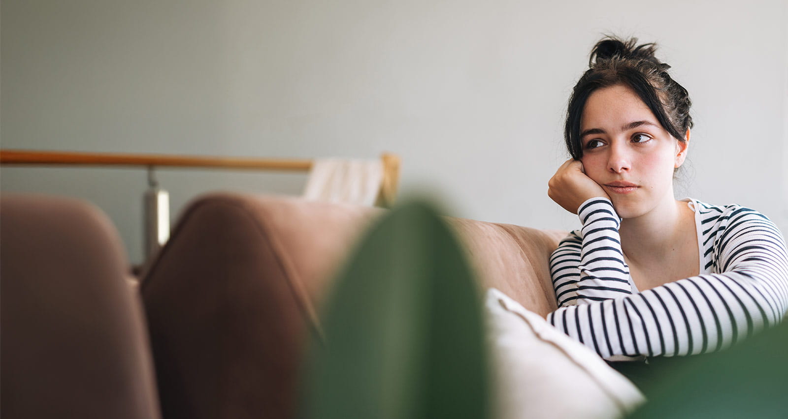 An upset teenage girl looking away and sitting in room at home