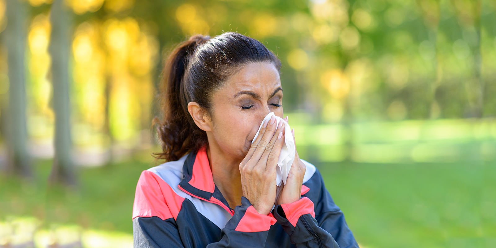 Woman coughing outside next to trees.