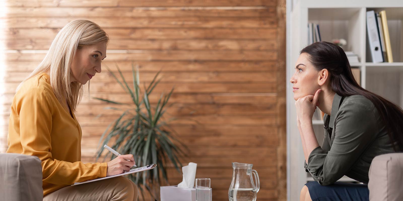 A psychologist taking notes on clipboard while sitting opposite the client