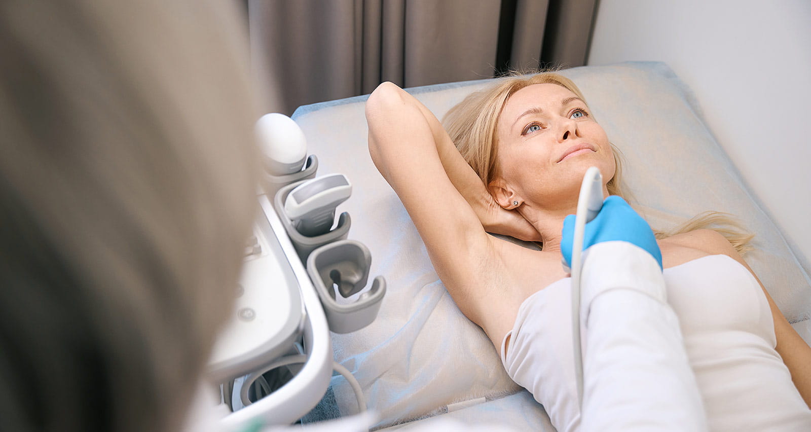 A medical specialist moves an ultrasonic sensor while performing a breast exam on a patient