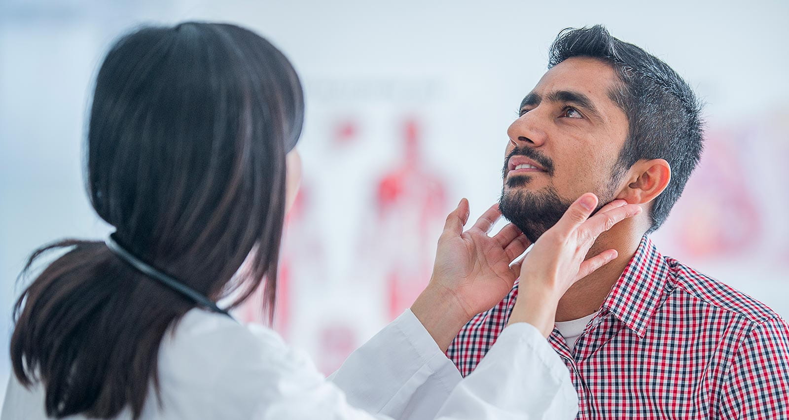 A provider examines a male patient’s throat for voice box cancer symptoms