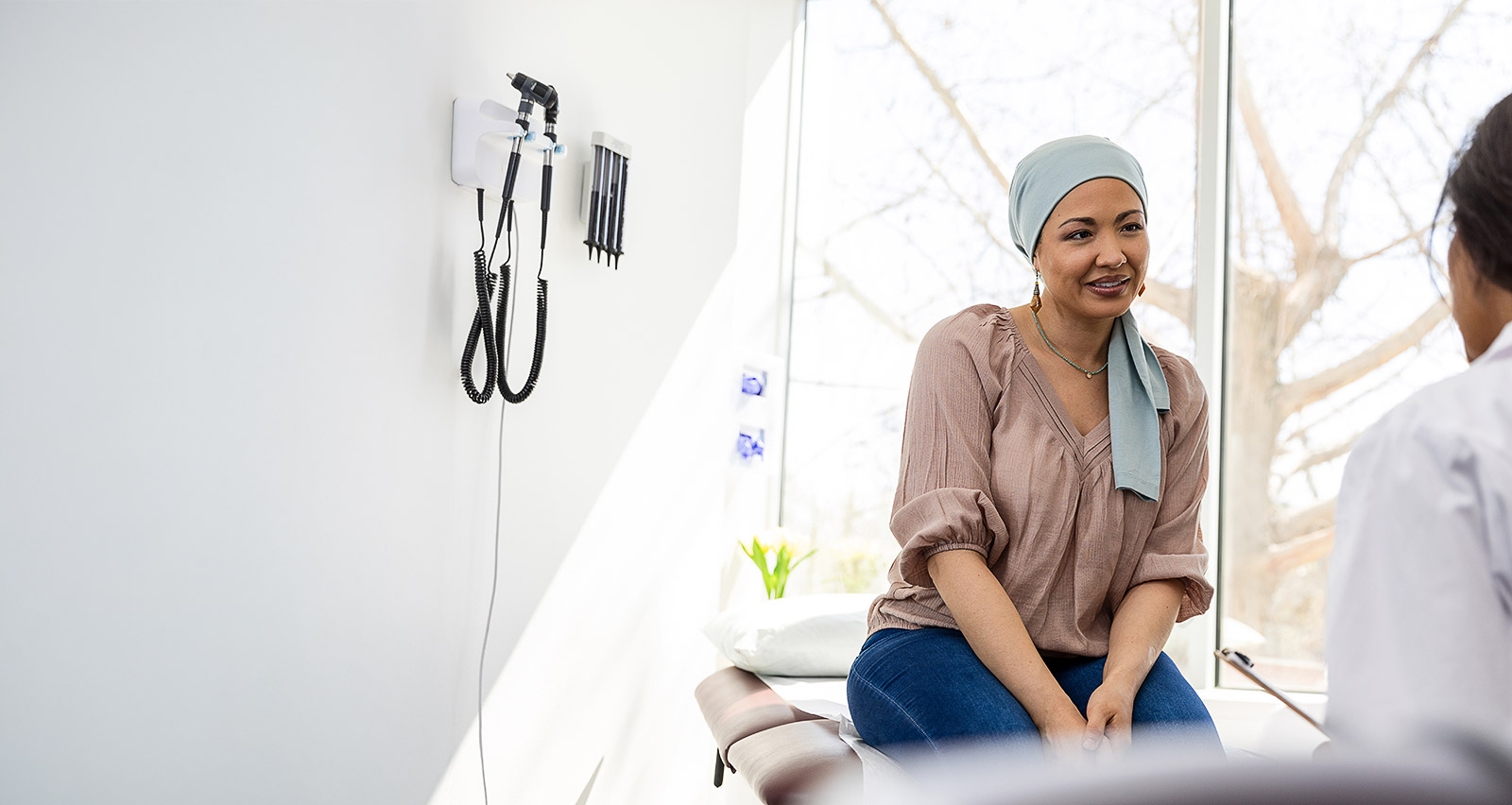 A female cancer patient wearing a headscarf consults with her provider in an exam room