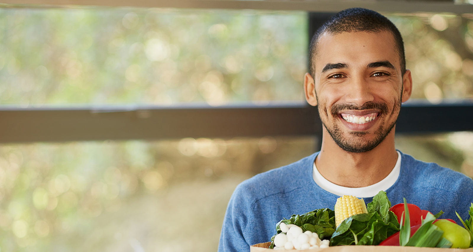 Portrait of a happy young man holding a bag full of healthy vegetables at home
