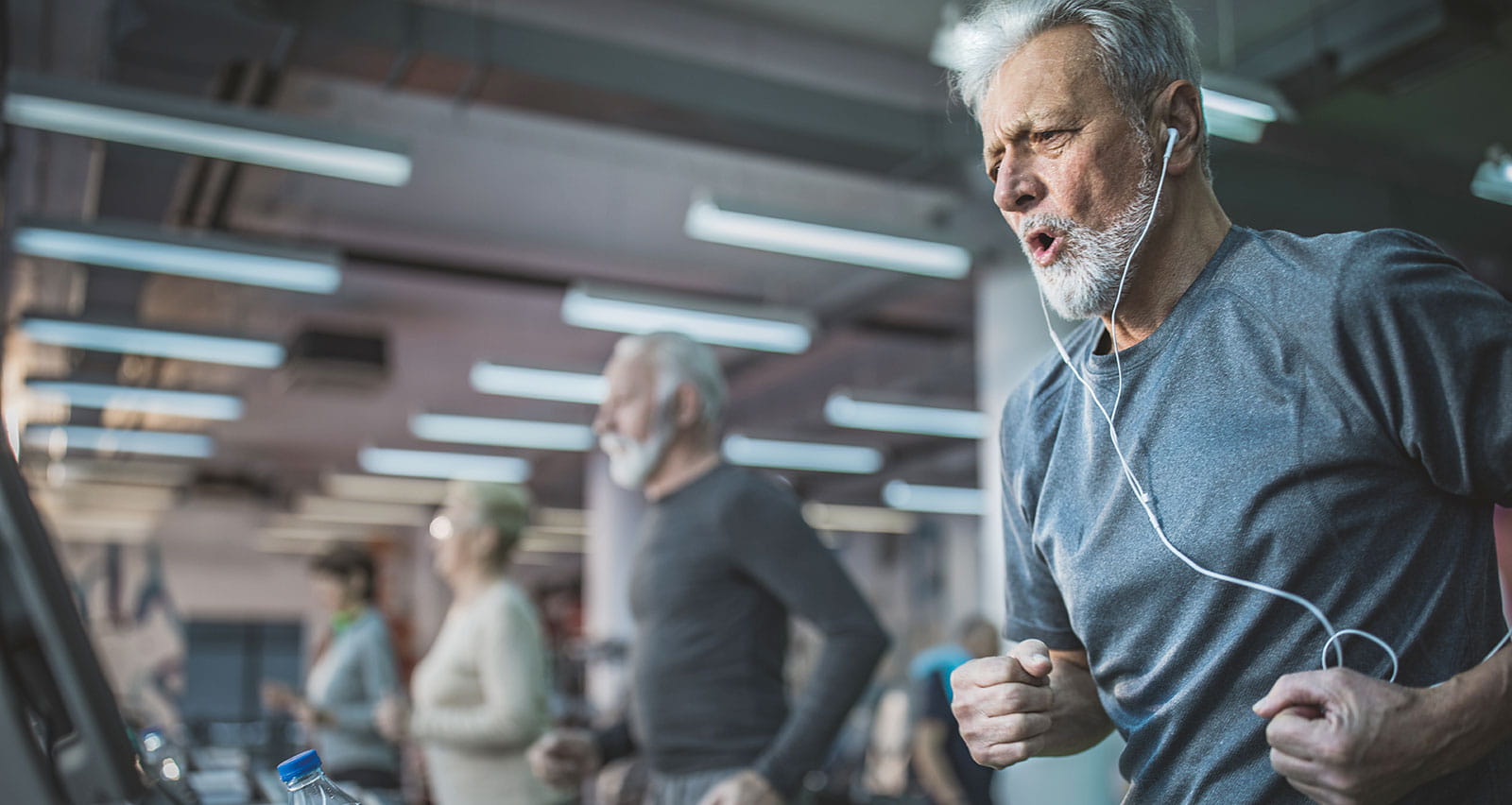 A determined mature man jogging on treadmill in a gym and listening music through earbuds