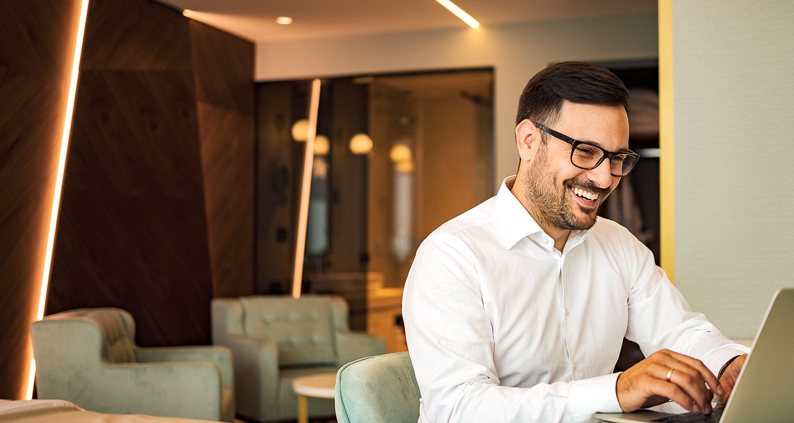 A happy businessman using a laptop in a hotel room