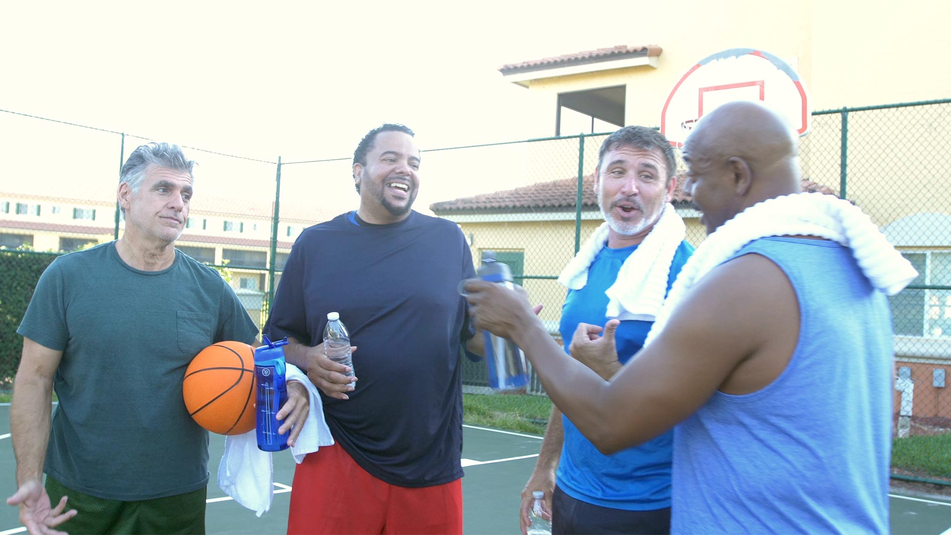 A multi-ethnic group of four middle-aged and senior men at a park playing basketball