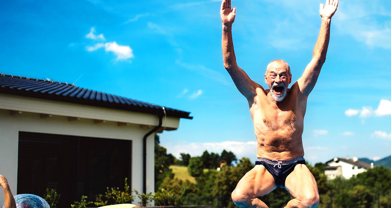 An older man smiles as he leaps into a swimming pool