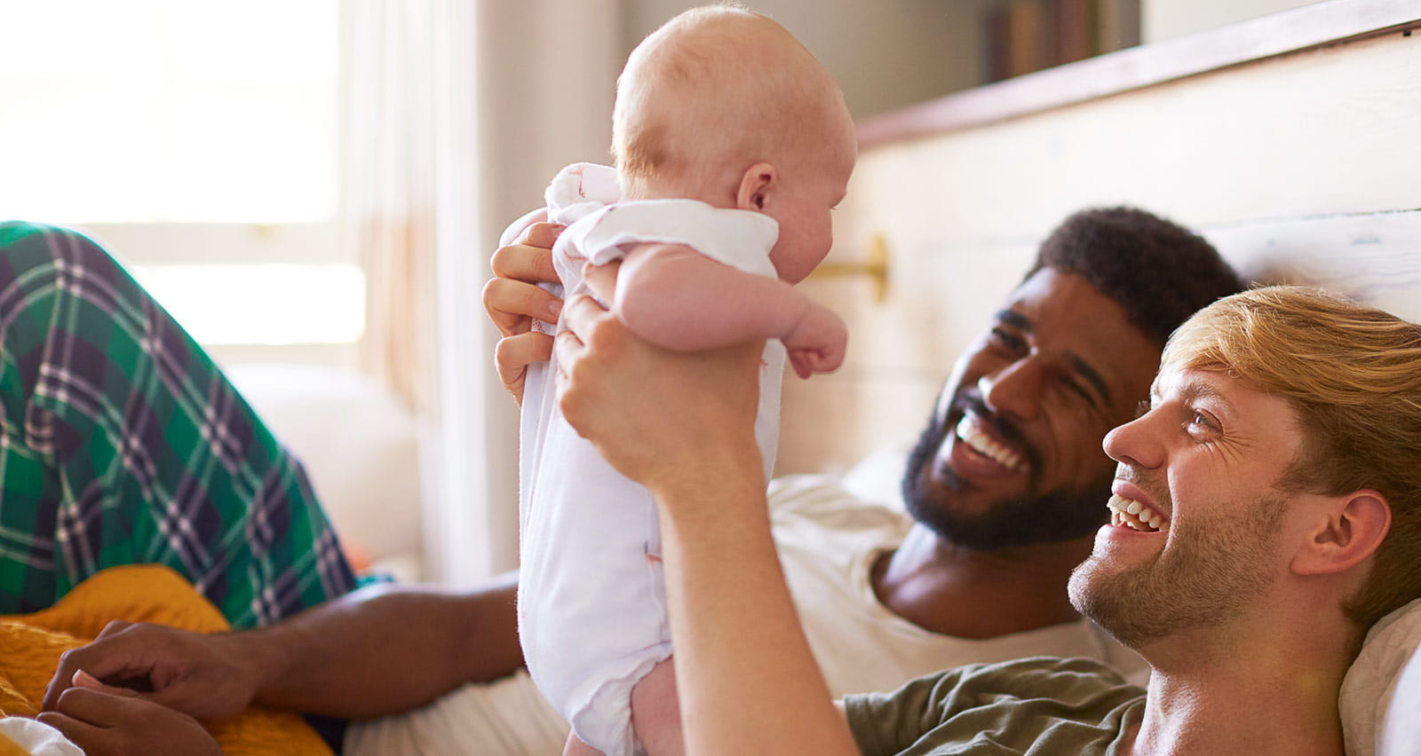 A loving male couple cuddling baby daughter in bedroom at home together