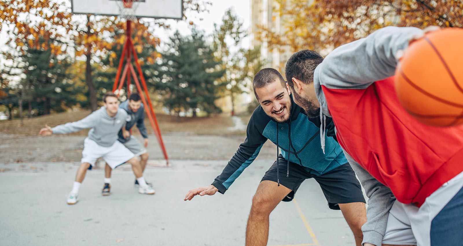 Four men play basketball on campus