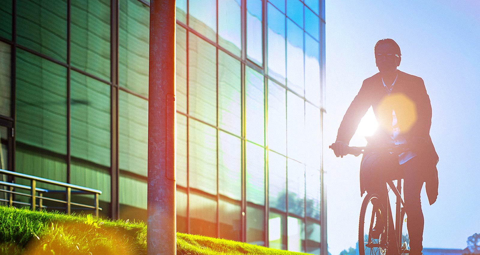 A man in business casual dress rides a bicycle beside a modern office building