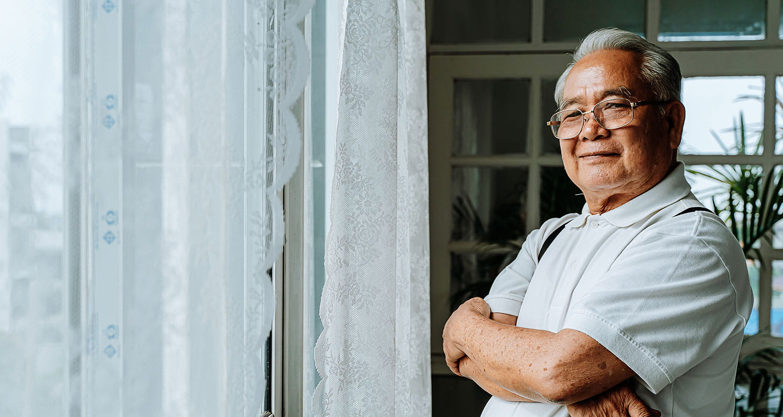 An older man looks outside his front window