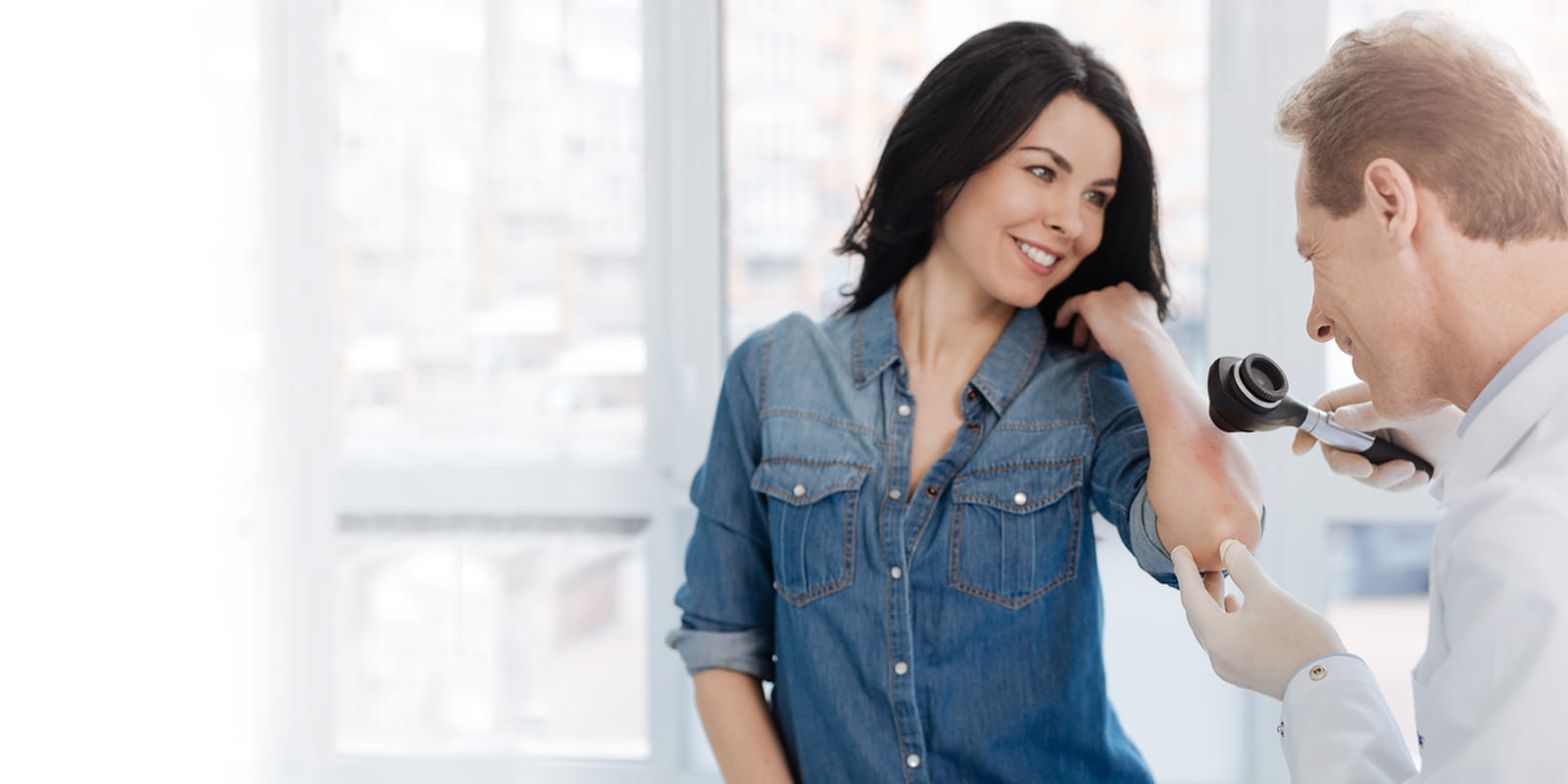 Dermatologist inspecting mole on female patient.