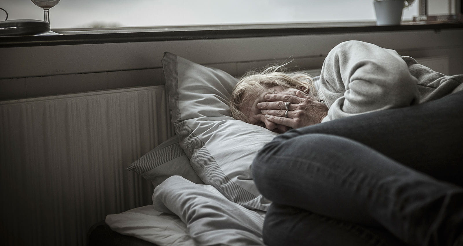 Older woman crouched atop bed, suffering from liver disease