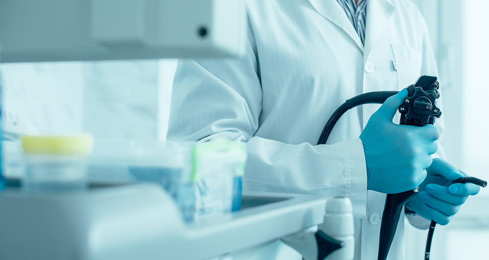 A male provider in white coat and rubber gloves standing with a modern endoscope in hand