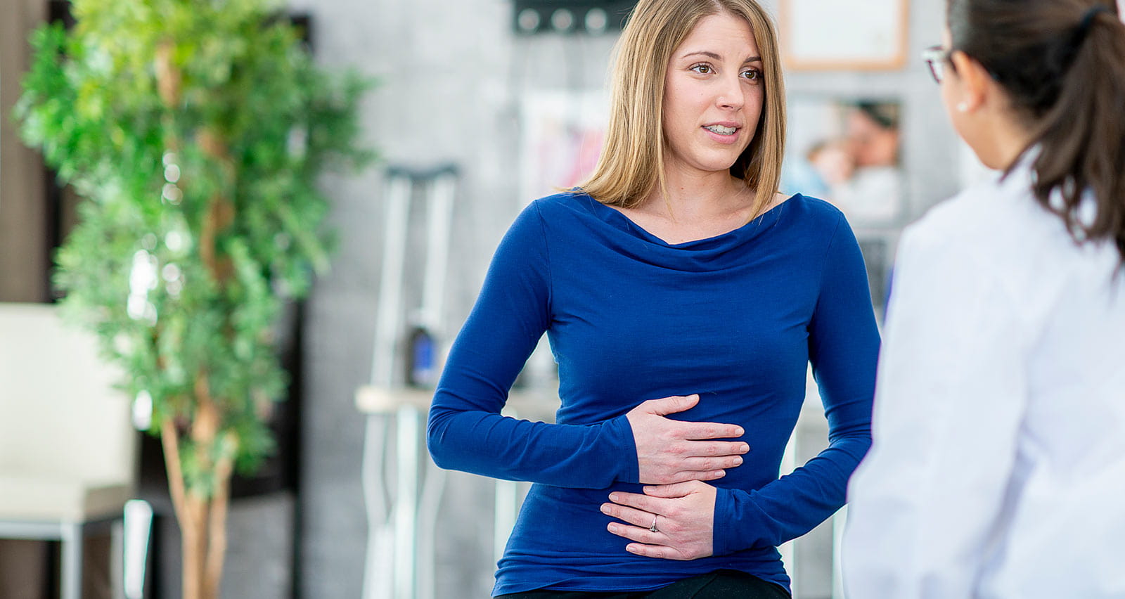 A woman is holding her stomach and describing her symptoms to a medical provider in an exam room