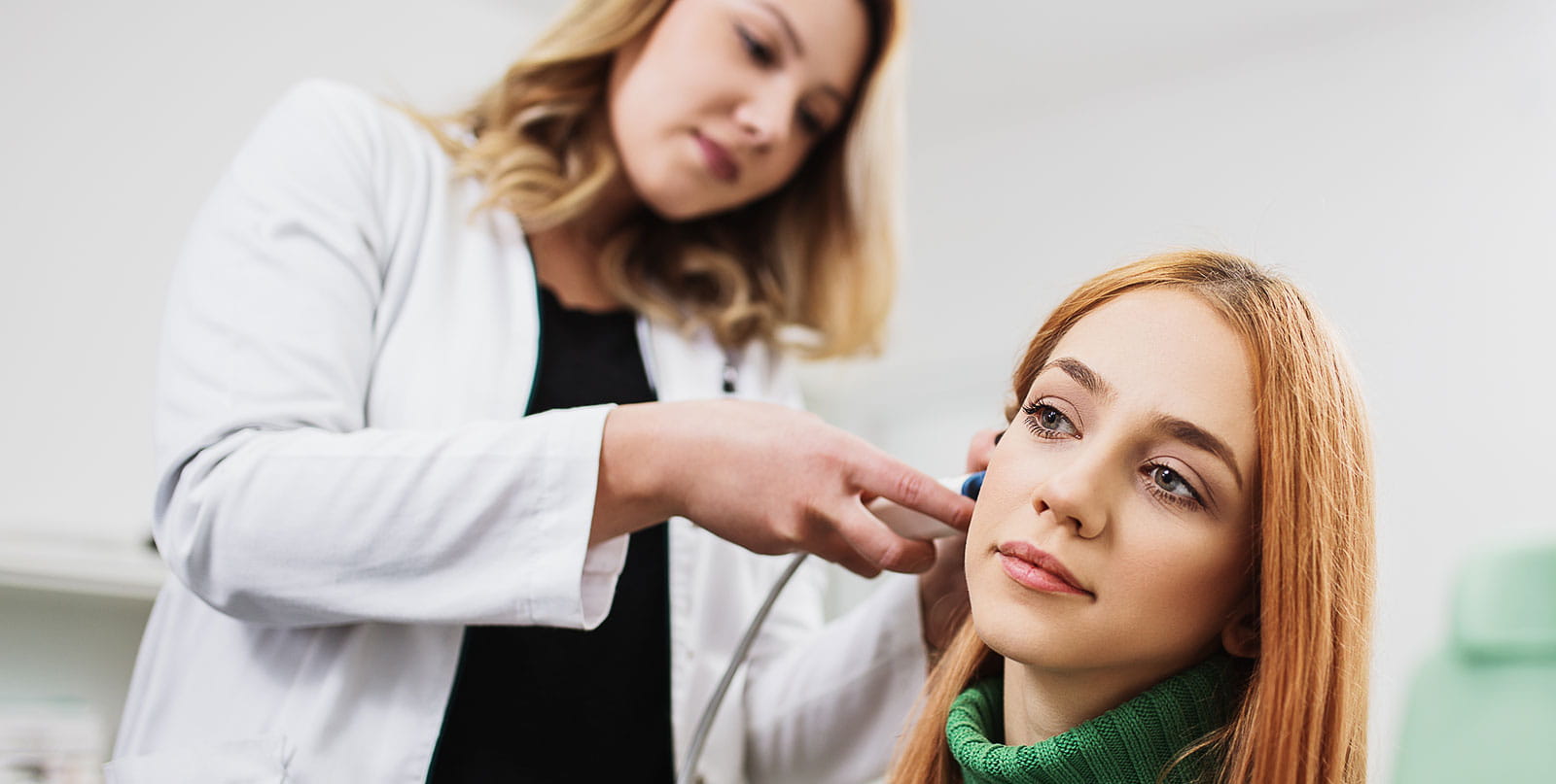 Young adult woman being examined with otoscope at otolaryngologist's office