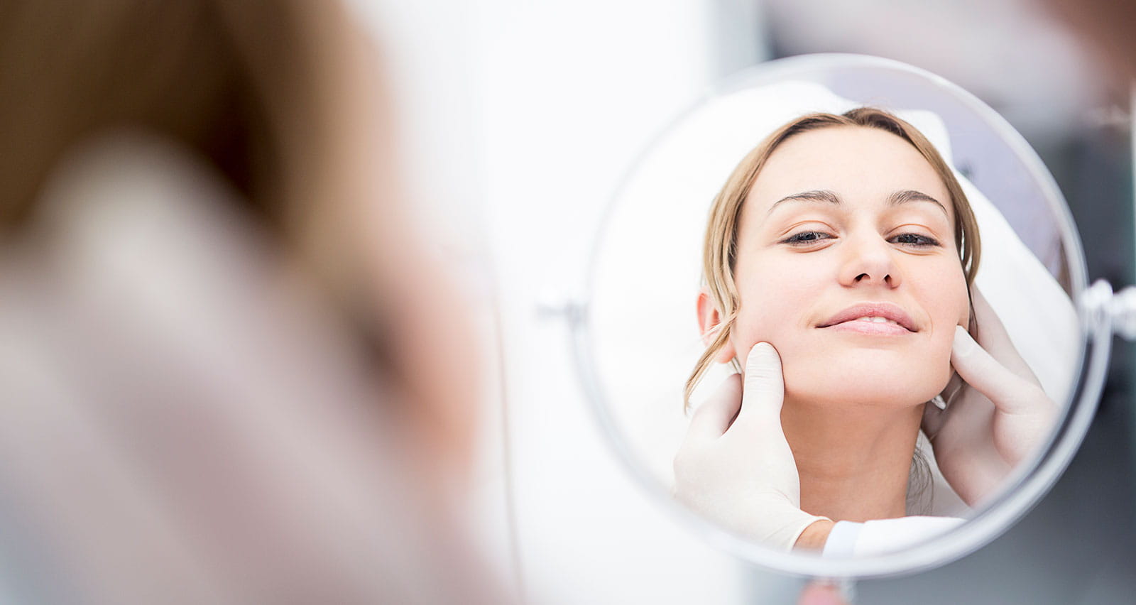 A woman looking in a mirror, reviewing the results of her aesthetic surgery