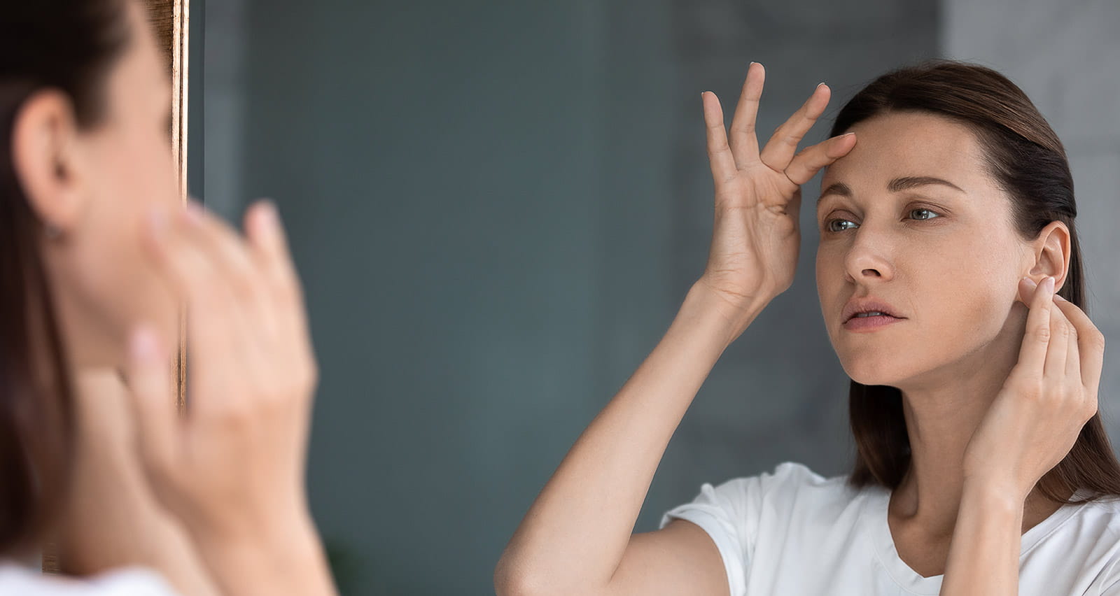 Anxious woman looking in mirror, touching forehead